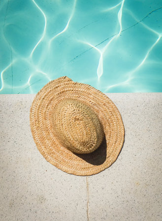 A vintage straw hat with sunglasses at the border of a swimming pool in summerの写真素材