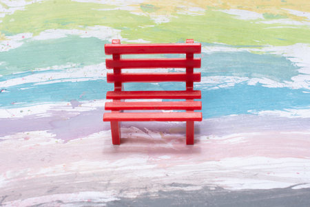A closeup of a small red bench on a painted colorful surfaceの写真素材