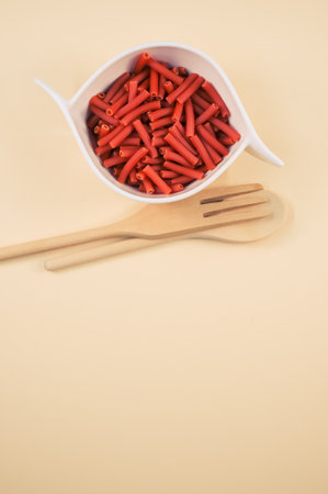 A bowl of macaroni pasta with a wooden spoon and fork isolated on a beige background with free space for textの写真素材