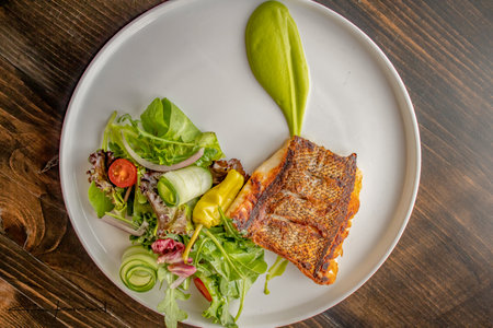 A top view of a fresh tasty grilled fish with a veggie salad on the plate