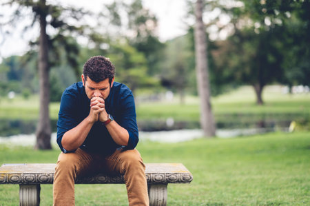 A young Caucasian man praying while sitting on a benchの写真素材