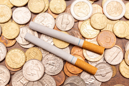 Two cigarette butts on coins depicting the concept of wasting money on harmful thingsの写真素材