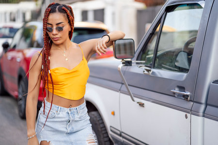 A closeup shot of a Hispanic woman with braids posing next to a car