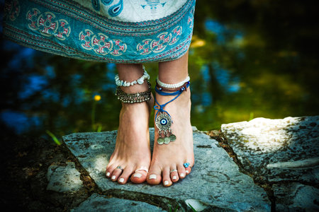 barefoot woman stand boho fashion style  with jewellery outdoor on stone close to pond close up shot...