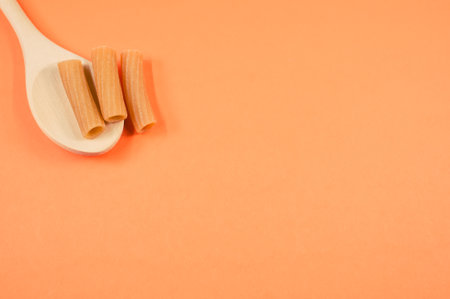 A top view shot of rigatoni on a spoon on an orange surface with free space for textの写真素材