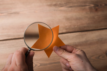 A person's hand holding a magnifying glass over the yellow paper cut in a star shapeの写真素材