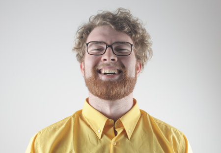 A portrait of an adult laughing Hungarian ginger man with a beard and glasses against a gray wallの写真素材