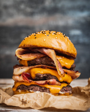 A close-up shot of a giant delicious mouthwatering burger with fried bacon, melted cheese, and beefの写真素材