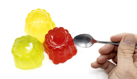 A closeup of three colorful jellies with a hand holding a spoon isolated on white background.