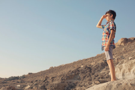 An Italian teenaged boy standing on cliffs and looking at the scenery while covering his eyes from the sun with his handの写真素材