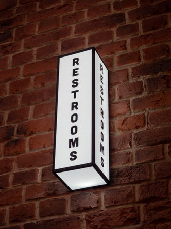 A vertical shot of a rectangular RESTROOMS sign with white led lights on the wallの写真素材