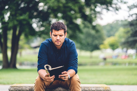 A thoughtful American man sitting on a park bench with a bookの写真素材