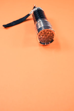 A vertical shot of a small black-silver flashlight isolated on an orange backgroundの写真素材