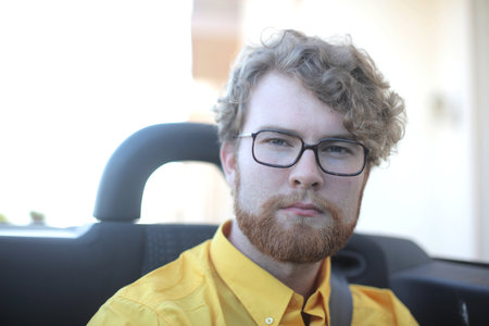 A portrait of a handsome ginger Hungarian man with glasses in a convertible car outdoors