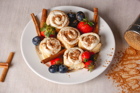 A closeup shot of delicious Cinnabons on the plate decorated with cinnamon sticks and berriesの写真素材