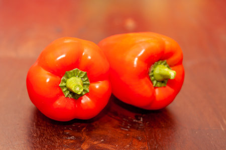 A close-up shot of two orange sweet Bulgarian peppers on a red wooden tableの写真素材