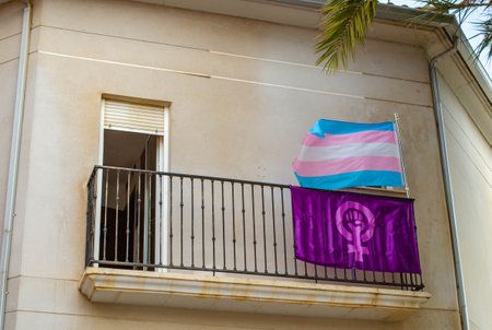A Waving Trans LGTB Flag and Purple Feminist Flag on a Balcony as a Form of Protestの写真素材