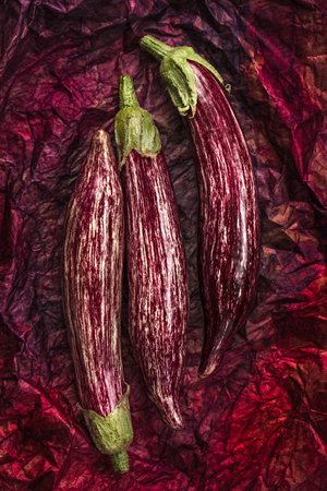 A vertical top view shot of three striped eggplants on wrinkled paperの写真素材