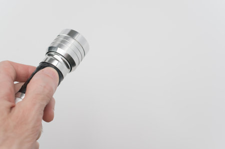 A hand of a male holding a small black-silver flashlight on a white backgroundの写真素材