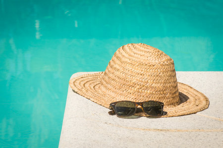 A vintage straw hat with sunglasses at the border of a swimming pool in summerの写真素材