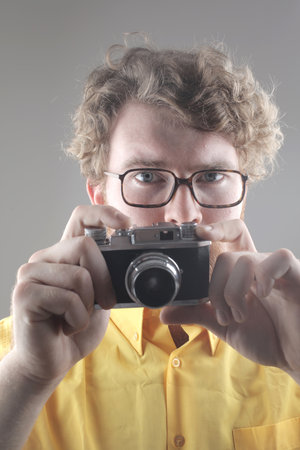 A portrait of an adult man with glasses taking a picture with a vintage cameraの写真素材