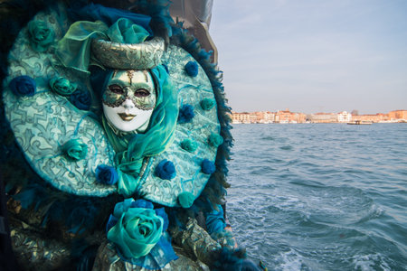 A female standing by the water in a mask and blue carnival costume under a clear sky in Venice, Italyの写真素材