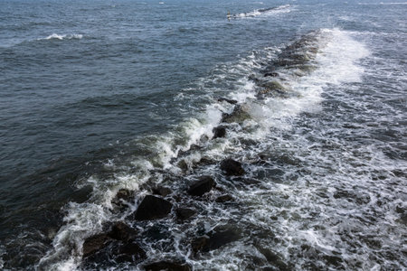 The Baltic Sea water washes over a breakwater made of stones and forms agitated and calm water.の写真素材