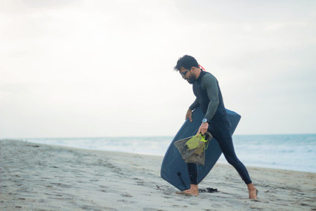 A scenic view of a Hispanic man on the beach with his surfboardの写真素材