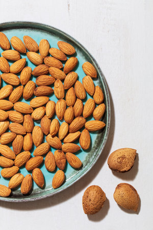 A vertical top view of almonds in a plate and in shell almonds next to itの写真素材