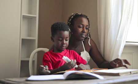 A portrait of a black kid doing his homework with his mother in front of the deskの写真素材