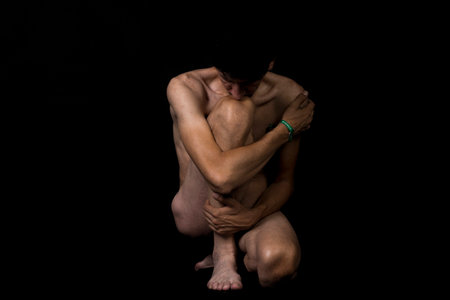 A closeup of a nude man curled and slouching with his hands on his feetの写真素材