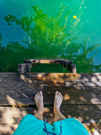 Point of view image of man standing on wooden deck over green lake or river.の写真素材