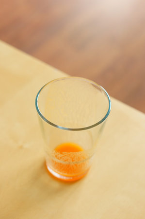 A vertical closeup shot of a dirty glass of orange juice isolated on the wooden tableの写真素材