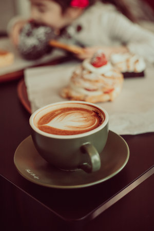 A close-up shot of a cup of fresh cappuccino with heart foam and a sweet pastry on the tableの写真素材