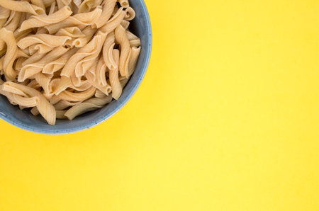 A bowl of cooked pasta on the upper left corner of a yellow background with copy spaceの写真素材