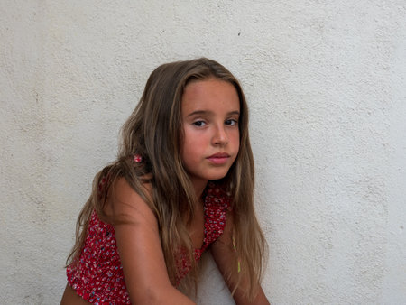 A cute teenage Caucasian girl with long hair isolated on a white concrete background looking at the cameraの写真素材
