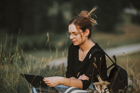 A shallow focus shot of a Bosnian Caucasian woman with a laptop in her lap outdoors in a fieldの写真素材