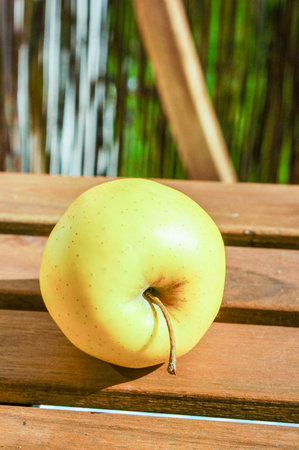 A vertical shot of a yellow apple on a wooden tableの写真素材
