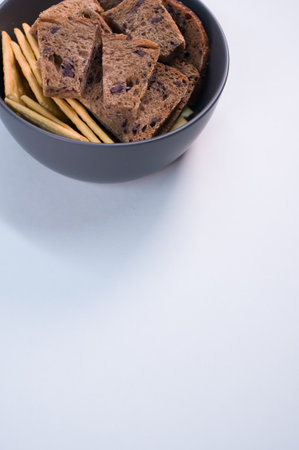 A closeup of the tasty salty crackers with slices of brown bread in the bowl on the blue  surfaceの写真素材