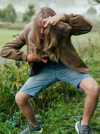 A long-haired Caucasian man wearing a jacket and shorts doing yoga in a foggy forest