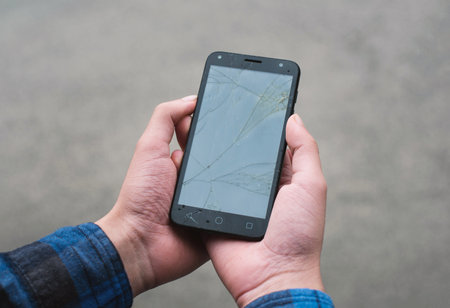 A closeup shot of a person's hand holding a cracked smartphone against a rusty wall background