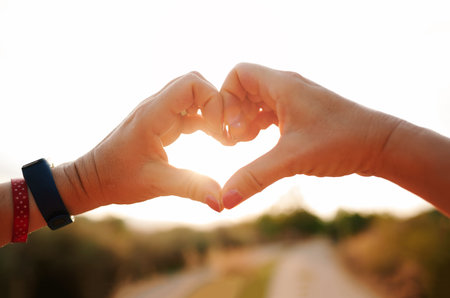 Two hands formulating a heart on a blurred background of a sunsetの写真素材