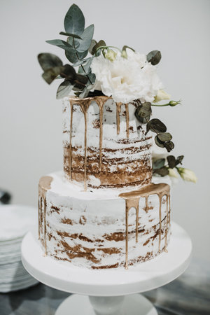 A vertical shot of a large white and gold wedding cake decorated with rosesの写真素材