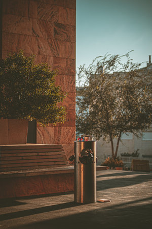 A vertical shot of a litter bin near a bench in a park under the sunlight