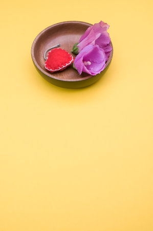 A close up of two velvet roses and red heart shape made of clothes in brown ceramic bowl on a yellow isolated backgroundの写真素材