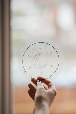 A vertical shot of Caucasian female hand holding a round transparent ornament sketch