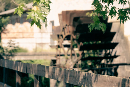 A selective focus of an old wooden railing of a bridge against a blurred watermillの写真素材