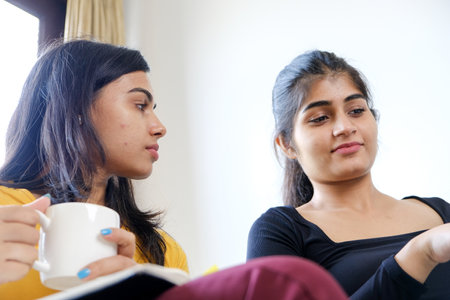 Two Indian best friends drinking coffee and discussing a movie while sitting on the couchの写真素材
