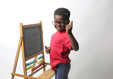 A portrait of an adorable black child pointing fingers near a tiny blackboard with an abacusの写真素材