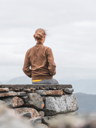 A scenic shot of a woman sitting on a cliff and looking at mountainsの写真素材